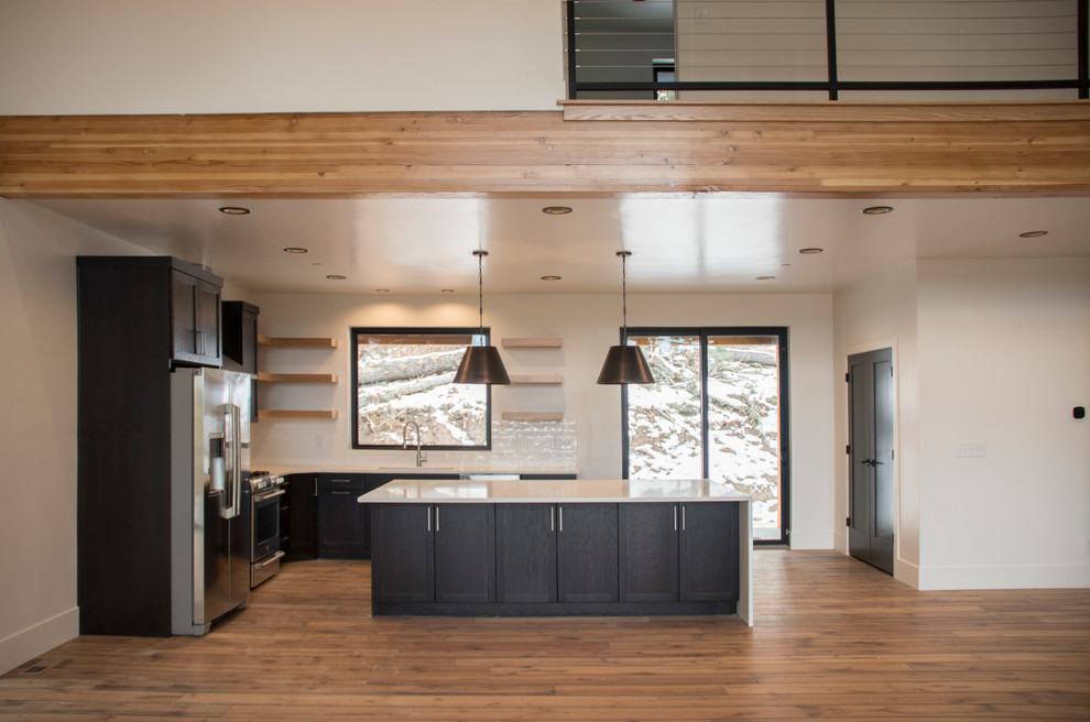 Design ideas for a medium sized modern l-shaped open plan kitchen in Salt Lake City with a submerged sink, shaker cabinets, black cabinets, engineered stone countertops, white splashback, ceramic splashback, stainless steel appliances, light hardwood flooring, an island and brown floors.