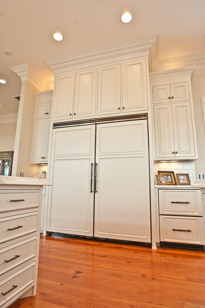 Foto på ett stort vit kök, med en undermonterad diskho, luckor med profilerade fronter, vita skåp, marmorbänkskiva, vitt stänkskydd, stänkskydd i tunnelbanekakel, rostfria vitvaror, mellanmörkt trägolv, en köksö och orange golv