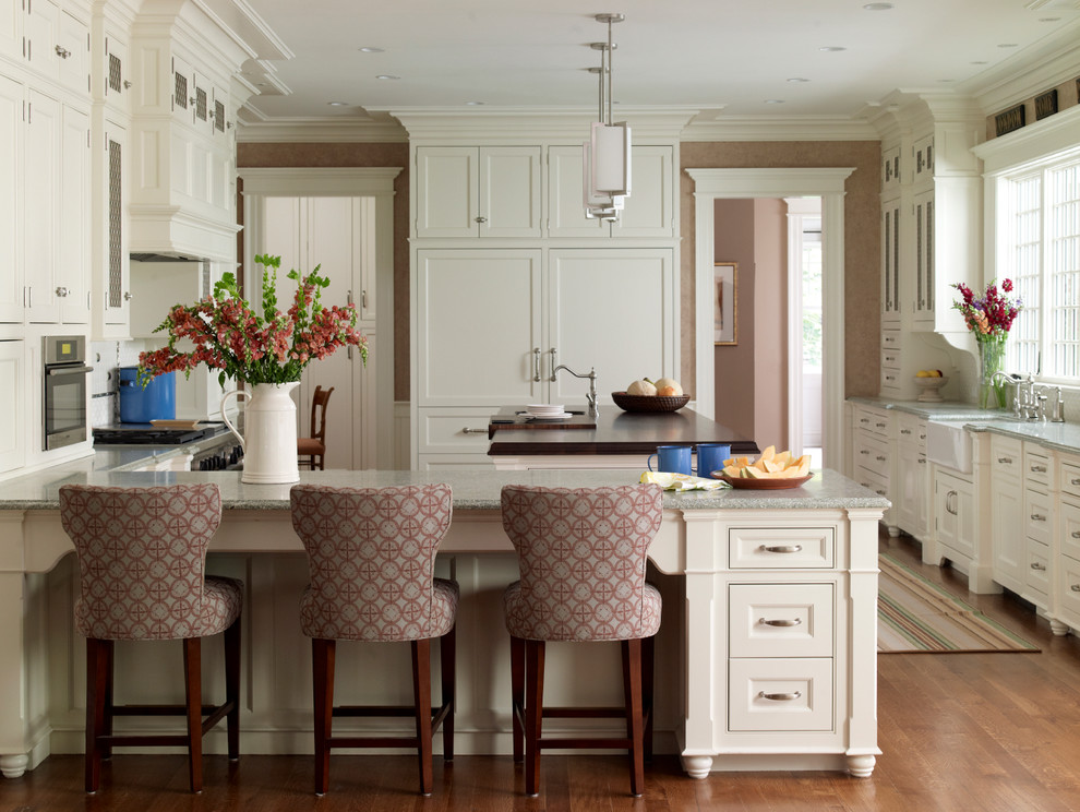 Klassische Küche in L-Form mit Landhausspüle, Schrankfronten mit vertiefter Füllung, weißen Schränken, Küchengeräten aus Edelstahl, braunem Holzboden und Kücheninsel in Miami