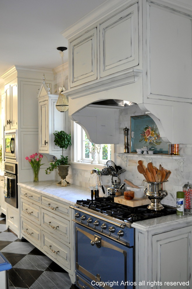 Elegant single-wall eat-in kitchen photo in Orlando with raised-panel cabinets, distressed cabinets, marble countertops, white backsplash, stone slab backsplash and colored appliances