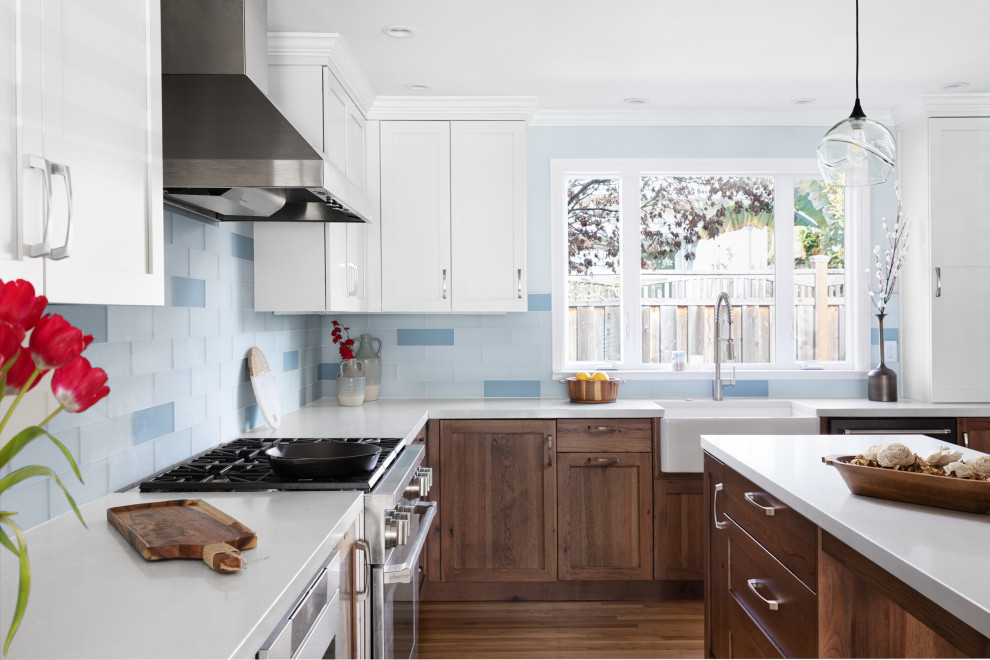 Foto på ett mellanstort maritimt vit kök, med en rustik diskho, luckor med infälld panel, skåp i slitet trä, bänkskiva i kvarts, blått stänkskydd, stänkskydd i glaskakel, rostfria vitvaror, mellanmörkt trägolv, en köksö och gult golv
