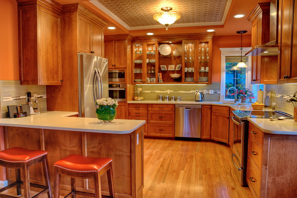 Bild på ett mellanstort vintage kök, med en undermonterad diskho, luckor med infälld panel, skåp i mellenmörkt trä, bänkskiva i kvarts, grönt stänkskydd, stänkskydd i glaskakel, rostfria vitvaror, mellanmörkt trägolv och en halv köksö
