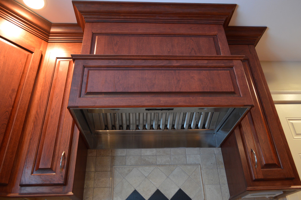 Medium sized traditional l-shaped kitchen in Boston with a submerged sink, raised-panel cabinets, dark wood cabinets, granite worktops, beige splashback, ceramic splashback, medium hardwood flooring and an island.