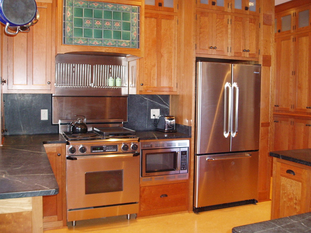 Klassisk inredning av ett kök, med en undermonterad diskho, skåp i shakerstil, skåp i mellenmörkt trä, bänkskiva i täljsten, svart stänkskydd, stänkskydd i sten, rostfria vitvaror, linoleumgolv och gult golv