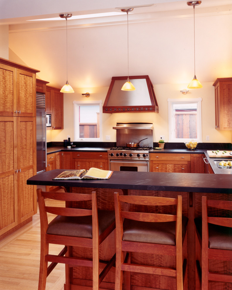 Cette image montre une cuisine traditionnelle en U et bois brun avec un électroménager en acier inoxydable, un évier encastré, un placard à porte shaker et un plan de travail en stéatite.