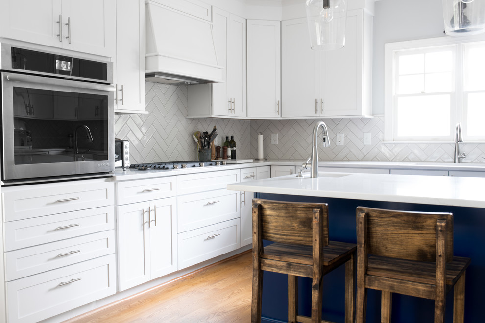 Bild på ett mellanstort vintage vit vitt kök, med en dubbel diskho, skåp i shakerstil, blå skåp, bänkskiva i kvarts, vitt stänkskydd, stänkskydd i marmor, rostfria vitvaror, mellanmörkt trägolv, en köksö och brunt golv
