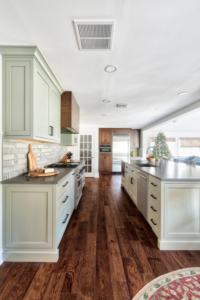 Exempel på ett mellanstort klassiskt grå grått kök, med en undermonterad diskho, gröna skåp, bänkskiva i kvarts, stänkskydd i keramik, rostfria vitvaror, en köksö, brunt golv, luckor med profilerade fronter, flerfärgad stänkskydd och mellanmörkt trägolv