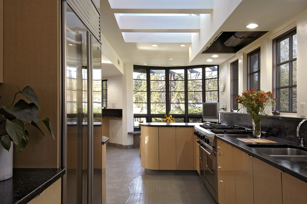 На фото: параллельная, отдельная кухня в современном стиле с техникой из нержавеющей стали, двойной мойкой, плоскими фасадами, светлыми деревянными фасадами и эркером с