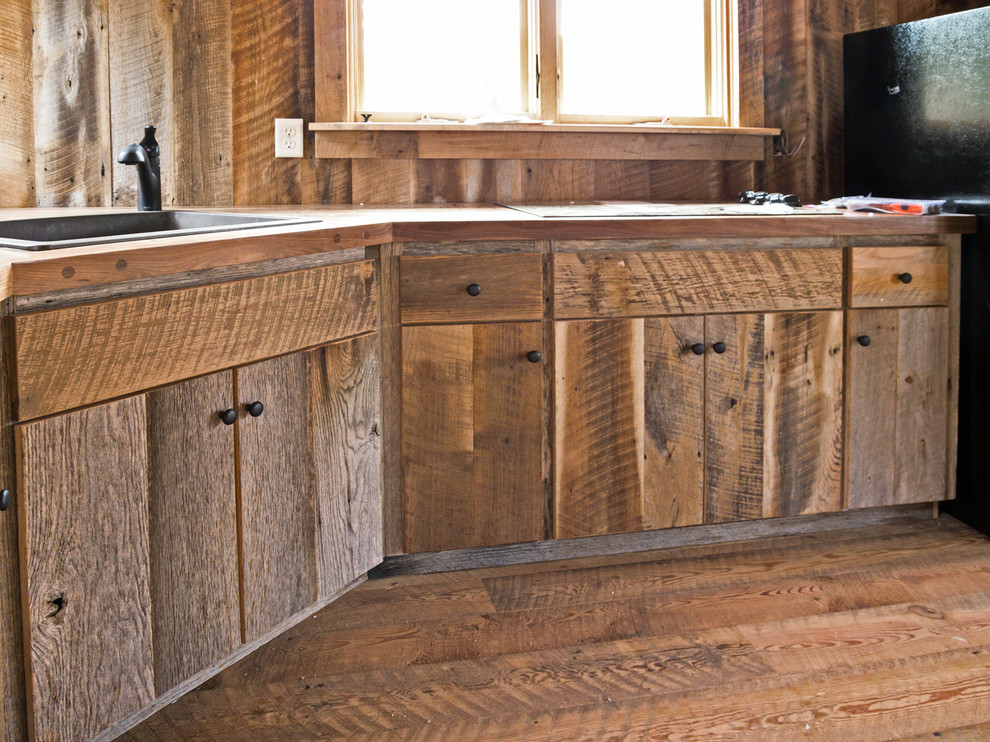 Exempel på ett mellanstort rustikt kök, med en nedsänkt diskho, släta luckor, skåp i slitet trä, träbänkskiva, brunt stänkskydd, stänkskydd i trä, svarta vitvaror och mellanmörkt trägolv