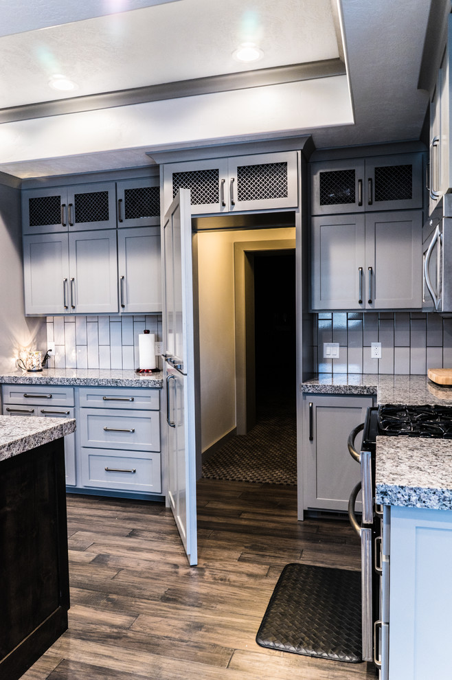 Große Moderne Küche mit grauen Schränken, Granit-Arbeitsplatte, Küchenrückwand in Weiß, Rückwand aus Keramikfliesen, Küchengeräten aus Edelstahl, braunem Holzboden, Kücheninsel und braunem Boden in Salt Lake City