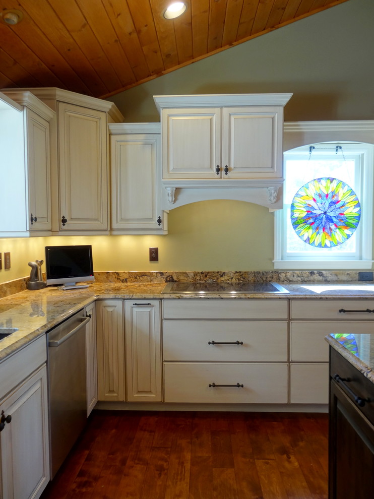 Inspiration for a large timeless l-shaped medium tone wood floor open concept kitchen remodel in Charlotte with an undermount sink, raised-panel cabinets, white cabinets, granite countertops, white backsplash, stainless steel appliances and an island