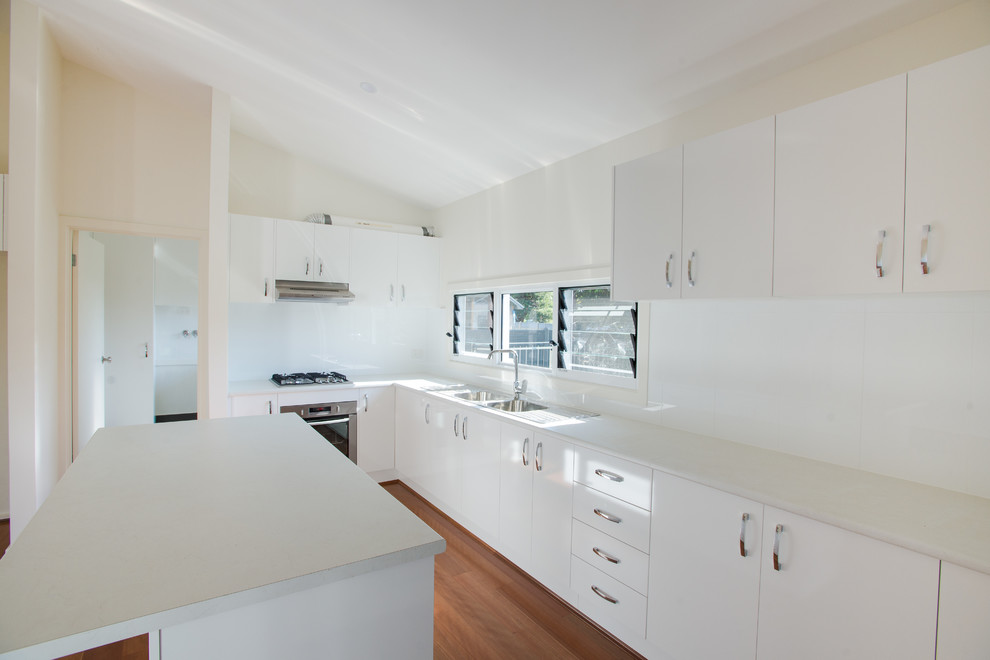 Bild på ett mellanstort funkis kök, med en dubbel diskho, vita skåp, laminatbänkskiva, vitt stänkskydd, stänkskydd i keramik, rostfria vitvaror och en köksö