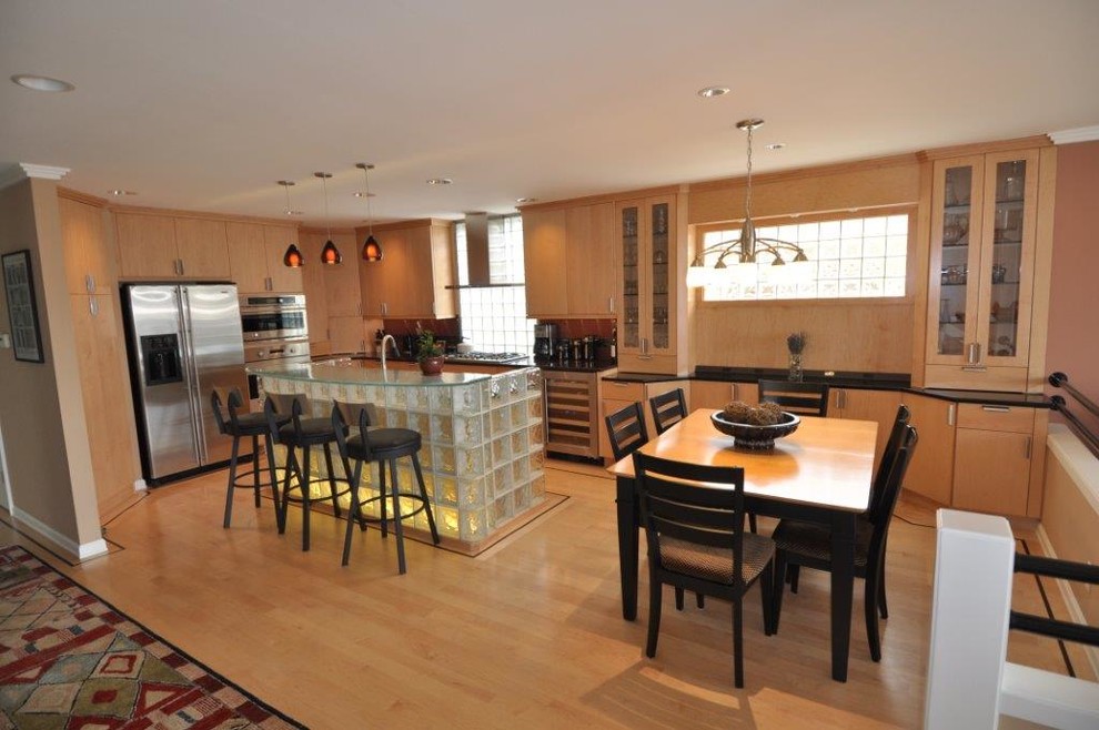 Mittelgroße Moderne Wohnküche in L-Form mit flächenbündigen Schrankfronten, hellen Holzschränken, Glas-Arbeitsplatte, Rückwand aus Glasfliesen, Küchengeräten aus Edelstahl, hellem Holzboden und Kücheninsel in Seattle