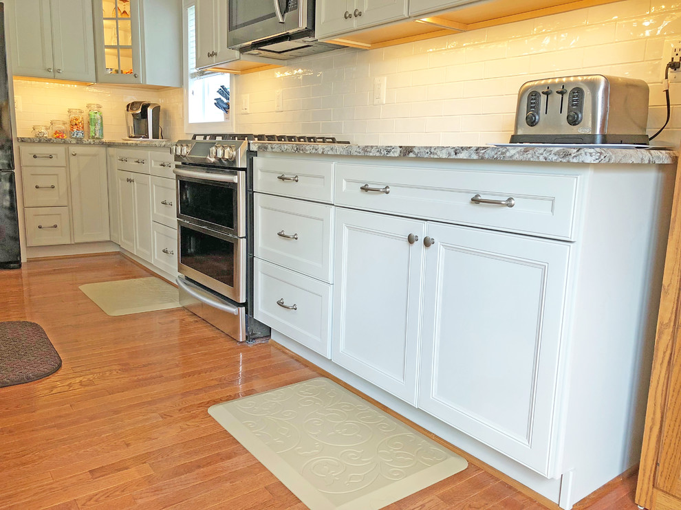 Foto på ett avskilt, mellanstort vintage grå l-kök, med en dubbel diskho, luckor med infälld panel, grå skåp, granitbänkskiva, vitt stänkskydd, stänkskydd i tunnelbanekakel, rostfria vitvaror, mellanmörkt trägolv, en köksö och brunt golv