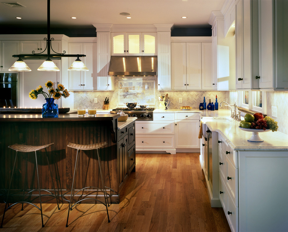 Large elegant l-shaped light wood floor and brown floor open concept kitchen photo in New York with a farmhouse sink, recessed-panel cabinets, white cabinets, marble countertops, white backsplash, ceramic backsplash, stainless steel appliances and an island