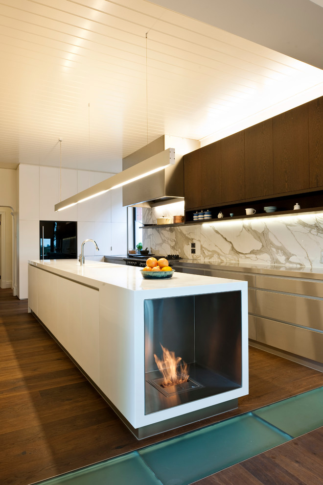 Diseño de cocina minimalista con armarios con paneles lisos, puertas de armario de madera en tonos medios, electrodomésticos negros, salpicadero de losas de piedra y salpicadero blanco