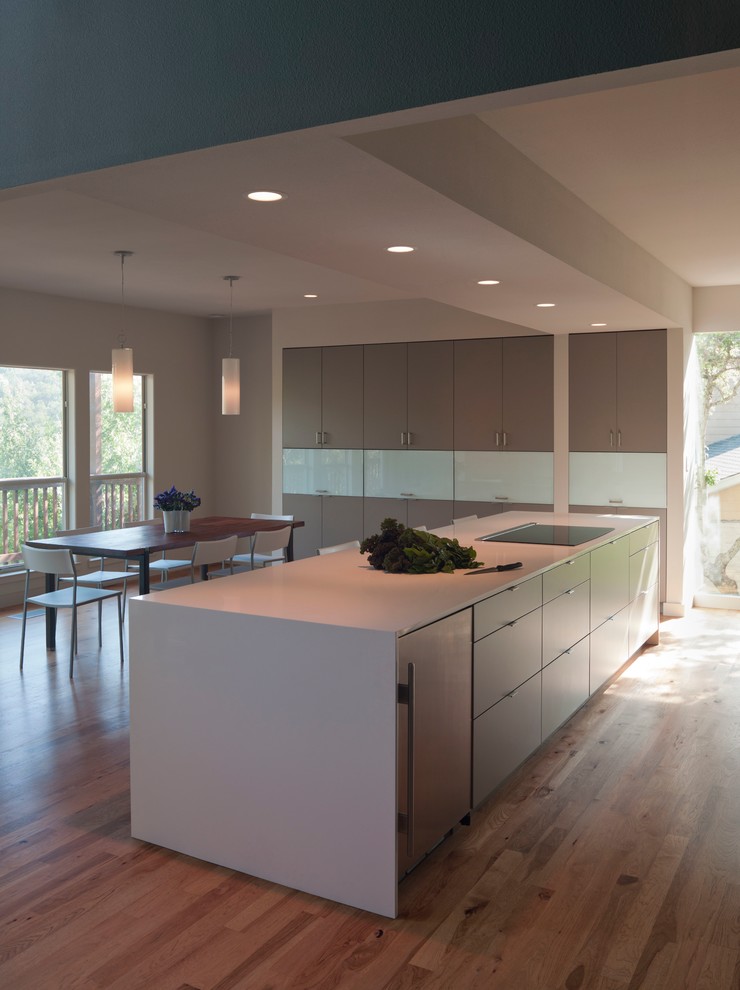 Example of a large minimalist galley open concept kitchen design in Austin with an undermount sink, flat-panel cabinets, gray cabinets, quartz countertops, white backsplash, glass sheet backsplash and stainless steel appliances