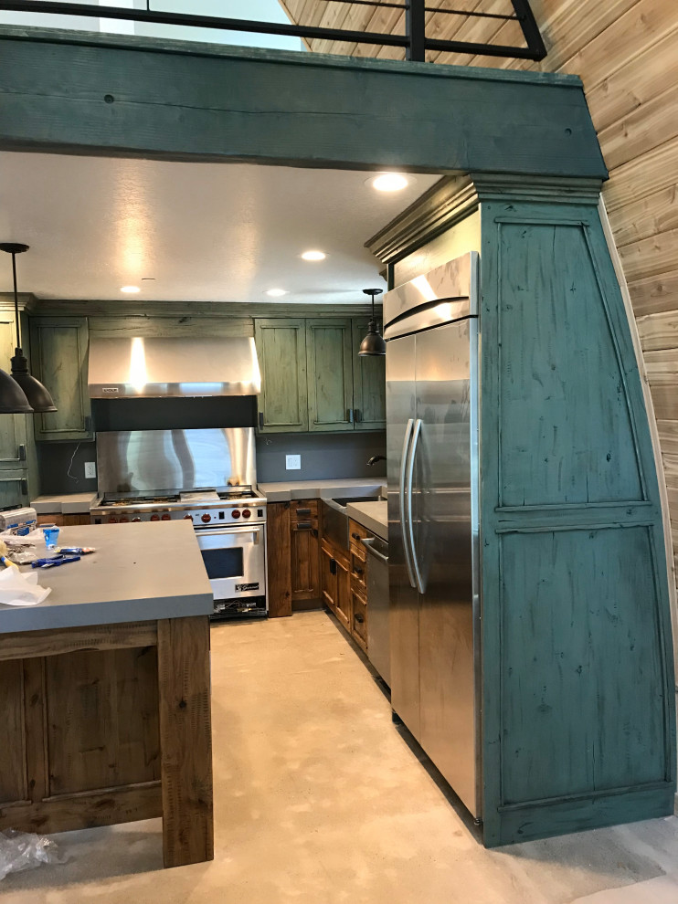 Example of a mid-sized mountain style l-shaped concrete floor and gray floor eat-in kitchen design with a farmhouse sink, shaker cabinets, green cabinets, quartz countertops, gray backsplash, stainless steel appliances, an island and gray countertops
