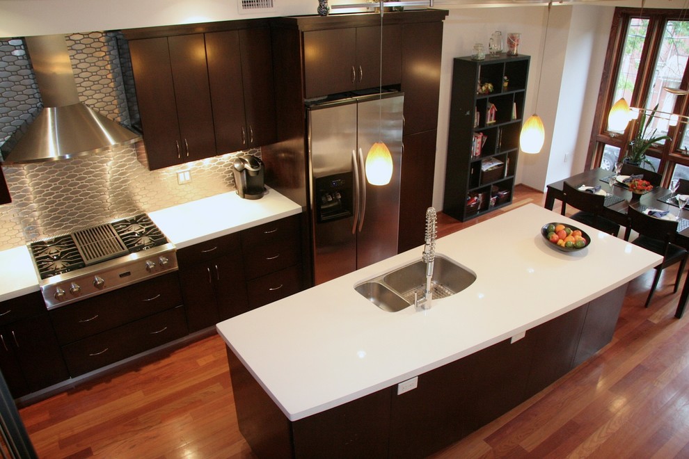 Example of a trendy single-wall open concept kitchen design in New York with an undermount sink, flat-panel cabinets, dark wood cabinets, solid surface countertops, metallic backsplash, metal backsplash and stainless steel appliances