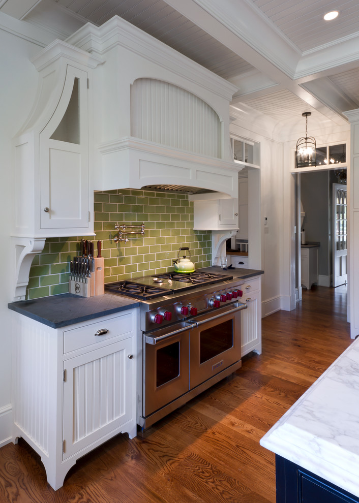 Foto på ett vintage kök och matrum, med vita skåp, bänkskiva i täljsten, grönt stänkskydd, stänkskydd i tunnelbanekakel, rostfria vitvaror, luckor med profilerade fronter och mellanmörkt trägolv