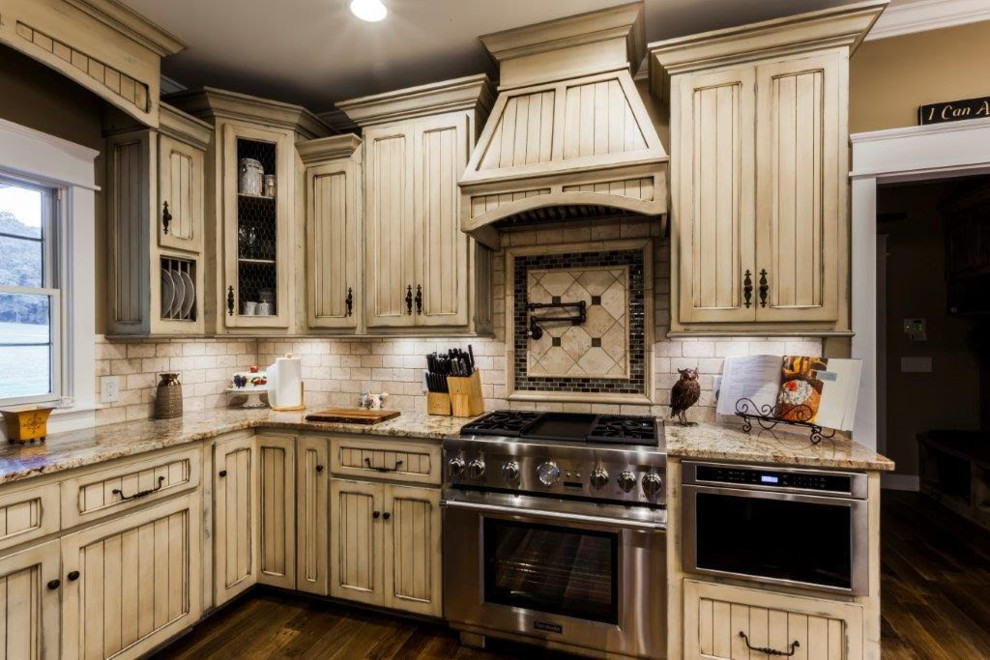 Lantlig inredning av ett mellanstort kök, med luckor med infälld panel, skåp i slitet trä, granitbänkskiva, vitt stänkskydd, stänkskydd i tunnelbanekakel, rostfria vitvaror, mörkt trägolv, en köksö och brunt golv