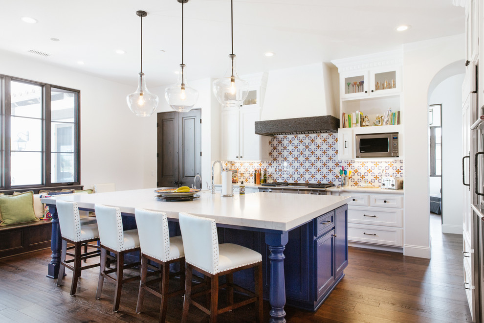 Mediterrane Küche in L-Form mit Schrankfronten mit vertiefter Füllung, weißen Schränken, bunter Rückwand, Küchengeräten aus Edelstahl, braunem Holzboden, Kücheninsel, braunem Boden und weißer Arbeitsplatte in San Luis Obispo