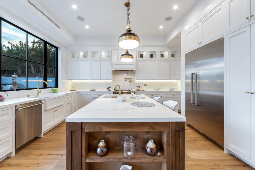 Eat-in kitchen - large transitional u-shaped light wood floor and beige floor eat-in kitchen idea in Los Angeles with a farmhouse sink, recessed-panel cabinets, white cabinets, quartzite countertops, white backsplash, stone slab backsplash, stainless steel appliances, an island and white countertops