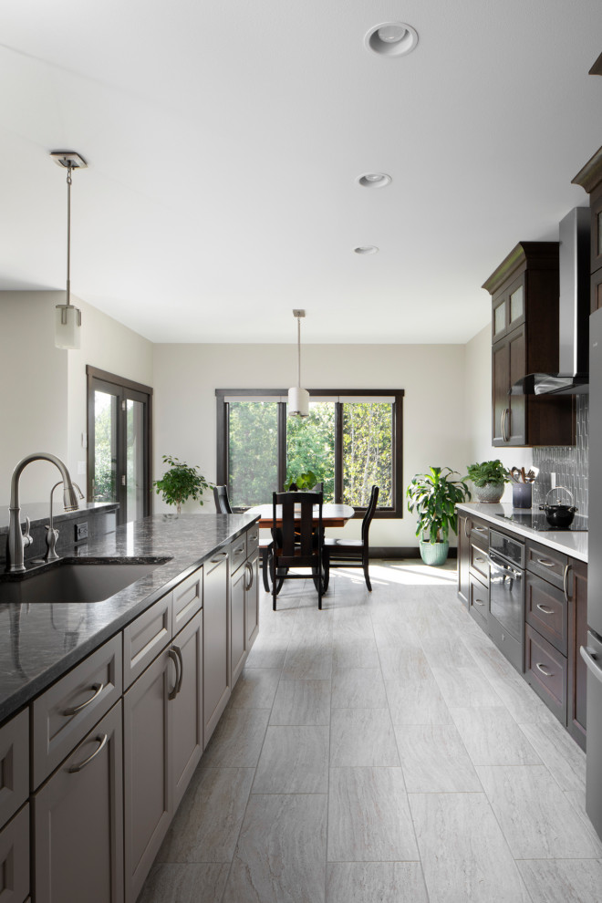 Inspiration for a mid-sized craftsman single-wall laminate floor and gray floor open concept kitchen remodel in Milwaukee with an undermount sink, shaker cabinets, dark wood cabinets, granite countertops, gray backsplash, ceramic backsplash, stainless steel appliances, no island and black countertops