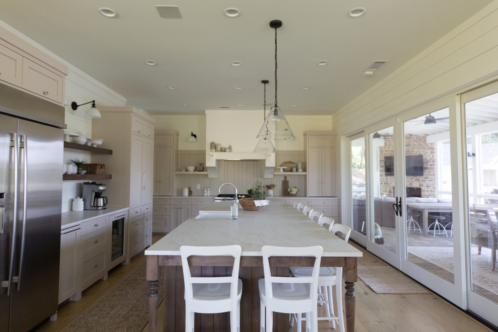 Inspiration for a farmhouse kitchen in Atlanta with shaker cabinets, beige cabinets, engineered stone countertops, beige splashback, tonge and groove splashback, stainless steel appliances, light hardwood flooring and an island.