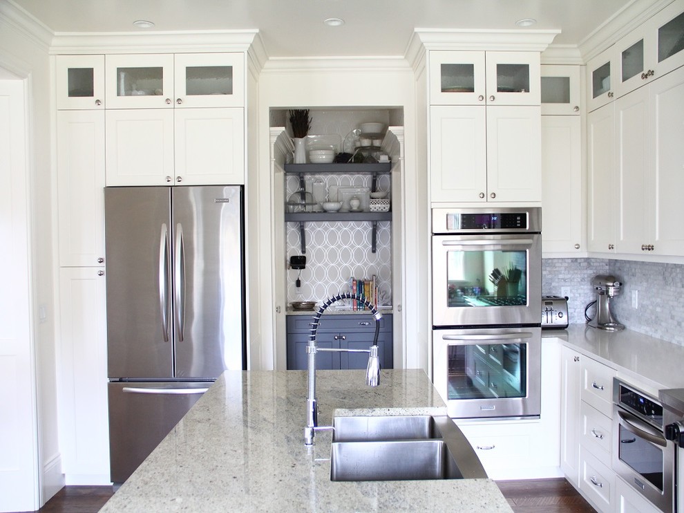 Foto på ett mellanstort vintage kök, med en undermonterad diskho, granitbänkskiva, grått stänkskydd, stänkskydd i stenkakel, rostfria vitvaror, en köksö, luckor med infälld panel, vita skåp, mörkt trägolv och brunt golv