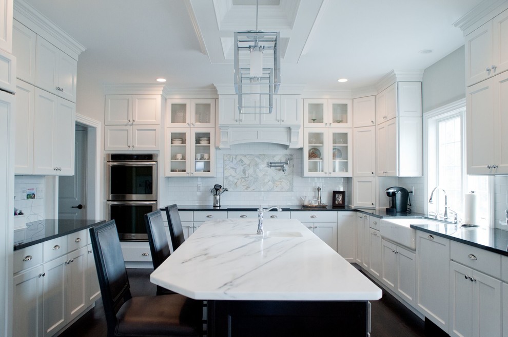 Modern inredning av ett stort flerfärgad flerfärgat kök, med en rustik diskho, luckor med infälld panel, vita skåp, marmorbänkskiva, vitt stänkskydd, stänkskydd i tunnelbanekakel, rostfria vitvaror, mörkt trägolv, en köksö och brunt golv