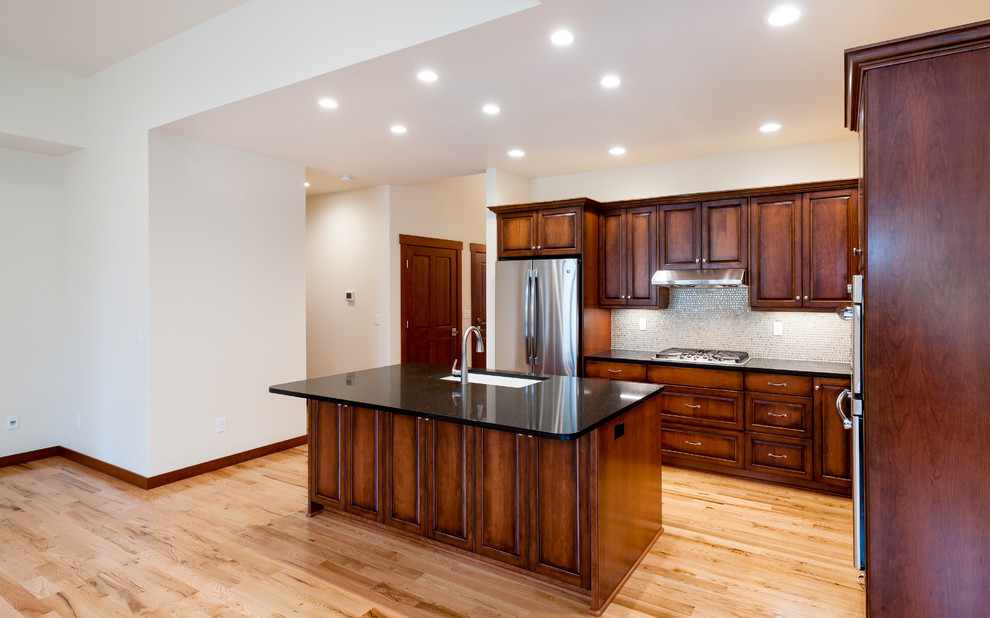 Example of a mid-sized classic l-shaped dark wood floor and brown floor open concept kitchen design in Seattle with an undermount sink, raised-panel cabinets, dark wood cabinets, granite countertops, beige backsplash, mosaic tile backsplash, stainless steel appliances and an island