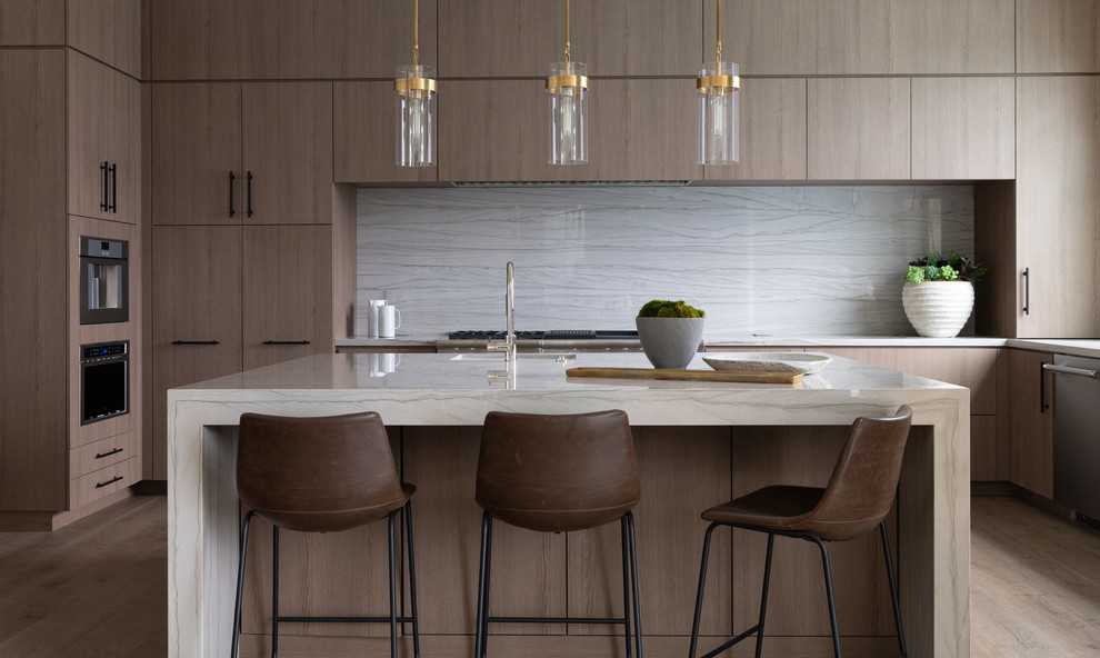 Moderne Küche in U-Form mit flächenbündigen Schrankfronten, hellen Holzschränken, Küchenrückwand in Weiß, Rückwand aus Stein, Küchengeräten aus Edelstahl, braunem Holzboden, Kücheninsel, braunem Boden und weißer Arbeitsplatte in Los Angeles