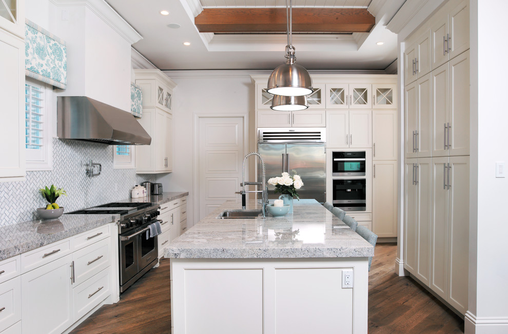 Inspiration for a large transitional u-shaped medium tone wood floor kitchen remodel in Miami with a drop-in sink, raised-panel cabinets, white cabinets, marble countertops, gray backsplash, ceramic backsplash and an island