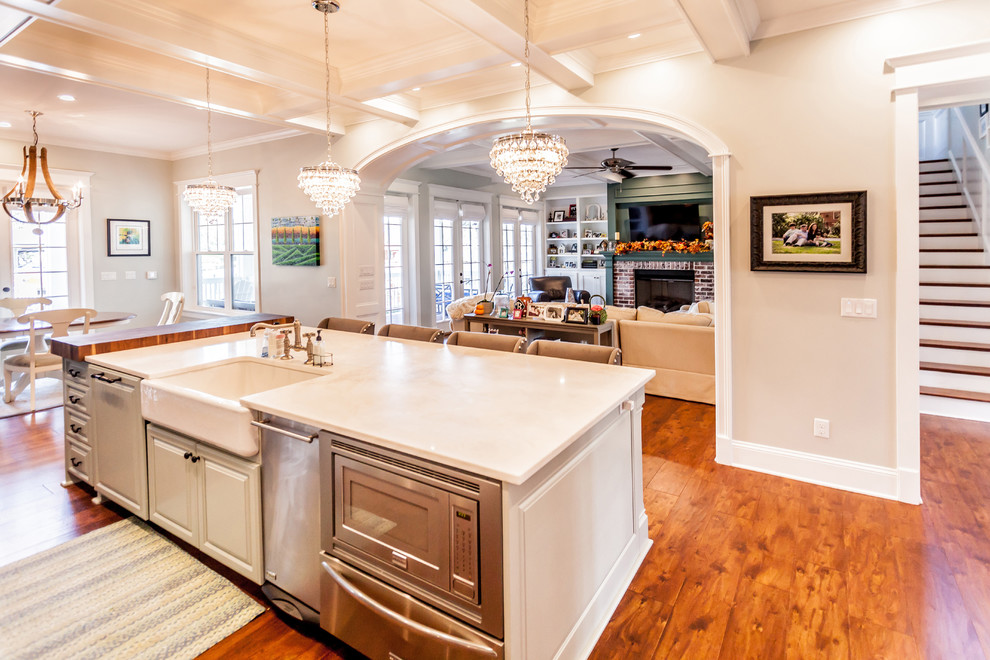 This is an example of a large contemporary galley open plan kitchen in Jacksonville with a belfast sink, raised-panel cabinets, white cabinets, granite worktops, stainless steel appliances, medium hardwood flooring, an island and brown floors.