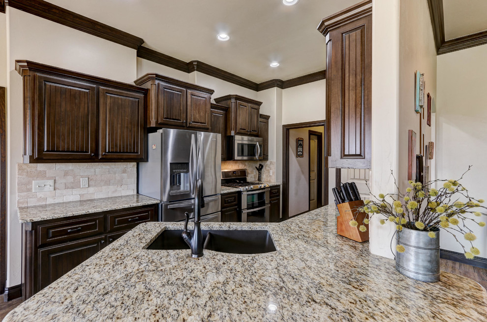Example of a mid-sized arts and crafts galley dark wood floor and brown floor eat-in kitchen design in Oklahoma City with an undermount sink, raised-panel cabinets, dark wood cabinets, granite countertops, beige backsplash, travertine backsplash, stainless steel appliances and a peninsula
