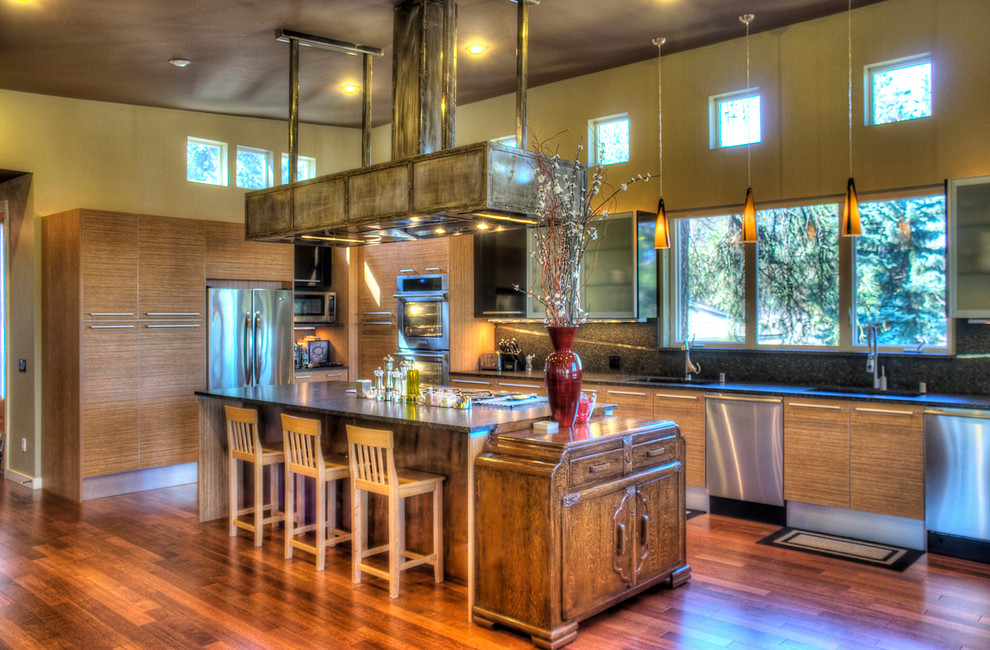 Cette image montre une grande cuisine ouverte design en U et bois brun avec un évier encastré, un placard à porte plane, un électroménager en acier inoxydable, un sol en bois brun, îlot et un sol marron.