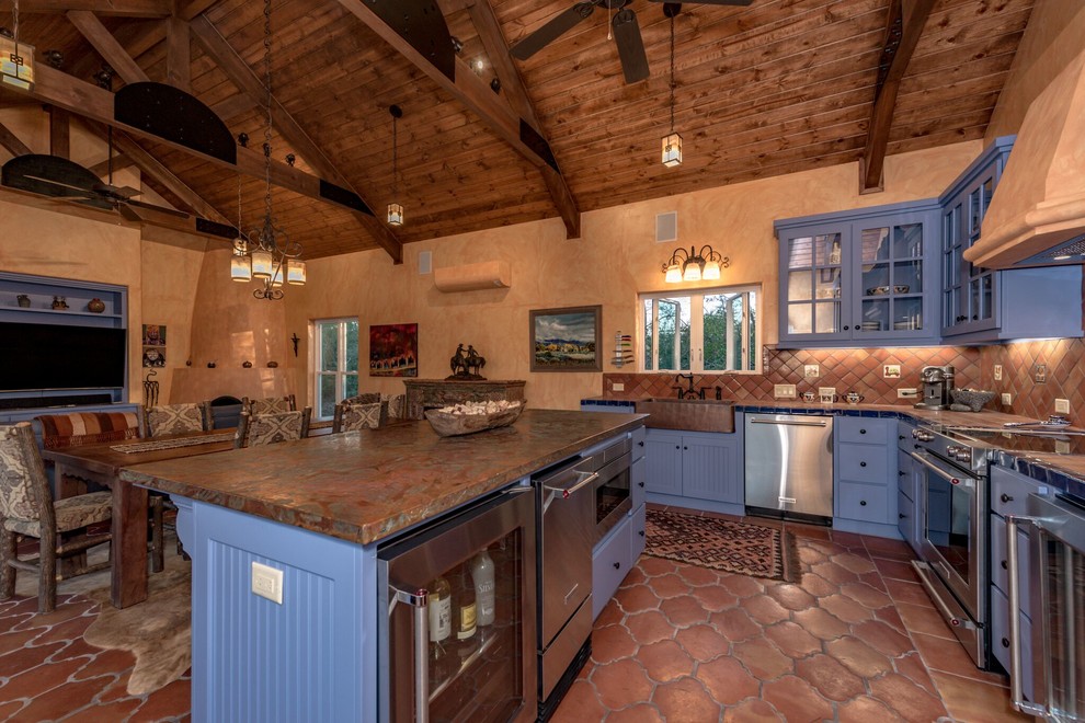 Open concept kitchen - mid-sized southwestern u-shaped terra-cotta tile and brown floor open concept kitchen idea in Austin with an undermount sink, flat-panel cabinets, blue cabinets, tile countertops, brown backsplash, terra-cotta backsplash, stainless steel appliances and an island