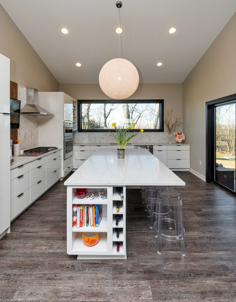 Foto på ett stort funkis kök, med släta luckor, vita skåp, stänkskydd i stenkakel, rostfria vitvaror, mörkt trägolv och en köksö