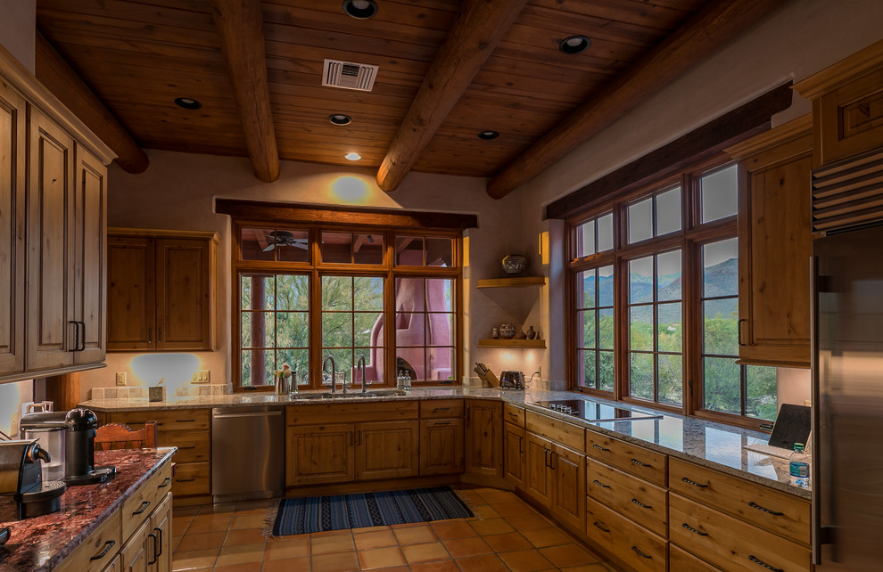Southwest terra-cotta tile and pink floor enclosed kitchen photo in Other with a triple-bowl sink, recessed-panel cabinets, brown cabinets, granite countertops, stainless steel appliances and no island