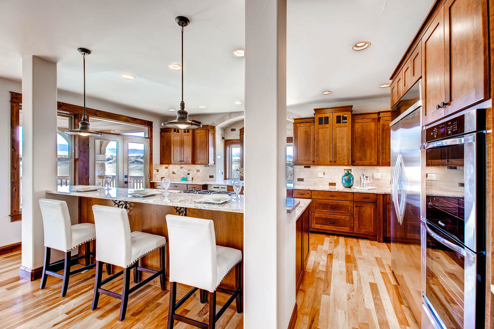 Example of an arts and crafts galley medium tone wood floor and brown floor eat-in kitchen design in Denver with a double-bowl sink, shaker cabinets, dark wood cabinets, granite countertops, beige backsplash, travertine backsplash, stainless steel appliances, an island and beige countertops