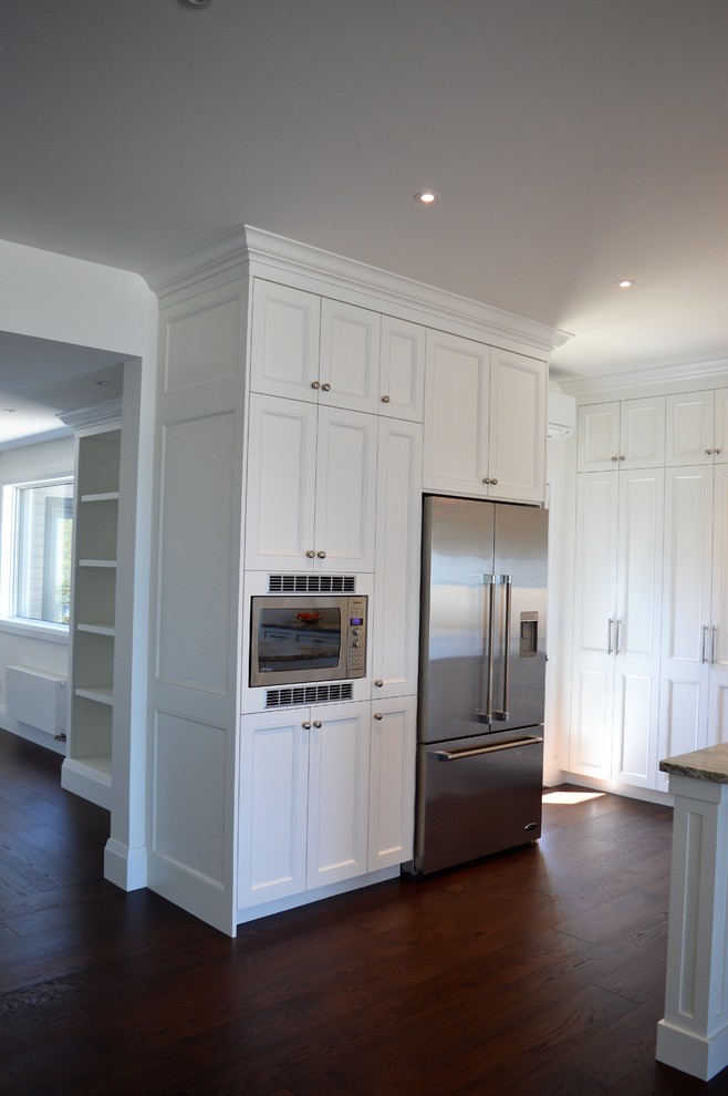 Photo of an expansive traditional l-shaped kitchen/diner in Toronto with a submerged sink, shaker cabinets, white cabinets, granite worktops, white splashback, ceramic splashback, stainless steel appliances, dark hardwood flooring, an island, brown floors and multicoloured worktops.