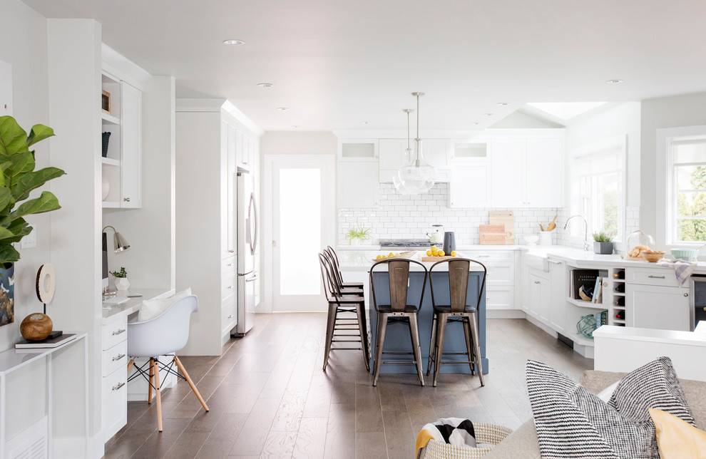 Design ideas for a large nautical l-shaped open plan kitchen in Vancouver with a belfast sink, shaker cabinets, white cabinets, engineered stone countertops, white splashback, stainless steel appliances, dark hardwood flooring, an island, brown floors and metro tiled splashback.