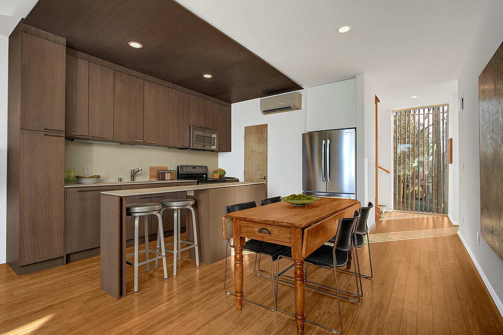 Diseño de cocina comedor lineal minimalista con armarios con paneles lisos, puertas de armario de madera en tonos medios y electrodomésticos de acero inoxidable