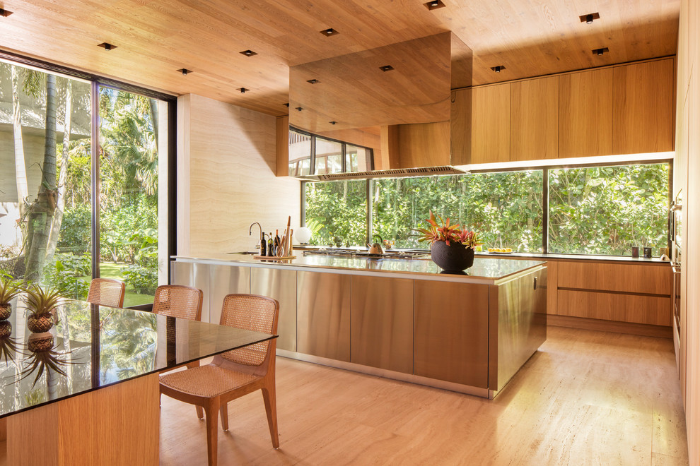Idee per un cucina con isola centrale tropicale con ante lisce, ante in legno chiaro, paraspruzzi a finestra, parquet chiaro e top in acciaio inossidabile