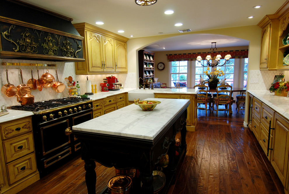 Idéer för ett avskilt klassiskt u-kök, med en rustik diskho, luckor med upphöjd panel, gula skåp, marmorbänkskiva, vitt stänkskydd, stänkskydd i tunnelbanekakel, svarta vitvaror, mellanmörkt trägolv och en köksö