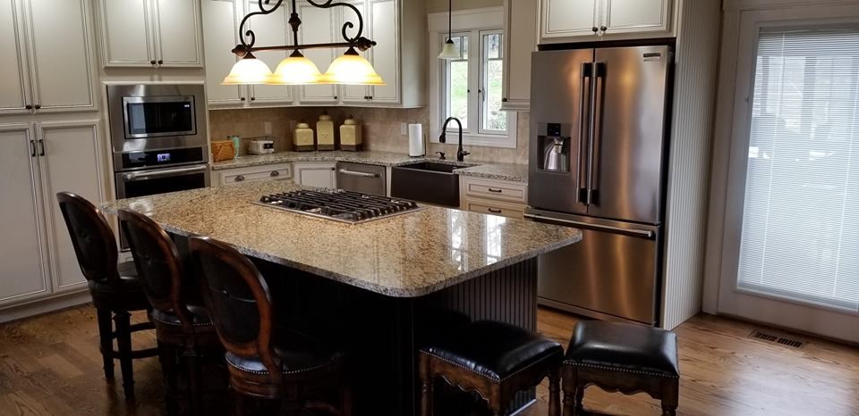 Mid-sized transitional l-shaped medium tone wood floor and brown floor eat-in kitchen photo in Other with a farmhouse sink, recessed-panel cabinets, white cabinets, granite countertops, beige backsplash, travertine backsplash, stainless steel appliances, an island and brown countertops