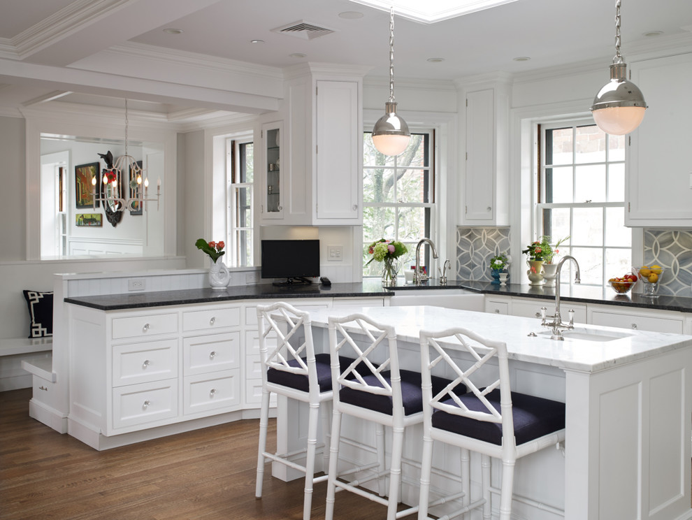 Example of a mid-sized trendy u-shaped medium tone wood floor and brown floor open concept kitchen design in Boston with a farmhouse sink, recessed-panel cabinets, white cabinets, granite countertops, gray backsplash, ceramic backsplash, stainless steel appliances and an island