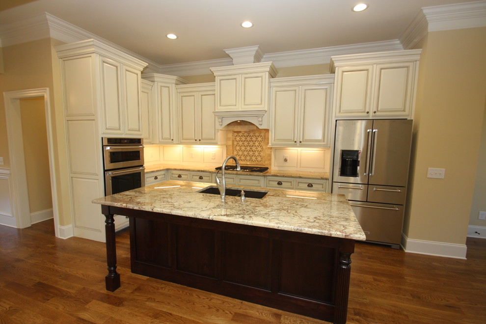 Example of a mid-sized classic l-shaped dark wood floor and brown floor open concept kitchen design in Raleigh with an undermount sink, raised-panel cabinets, white cabinets, granite countertops, beige backsplash, stainless steel appliances and an island