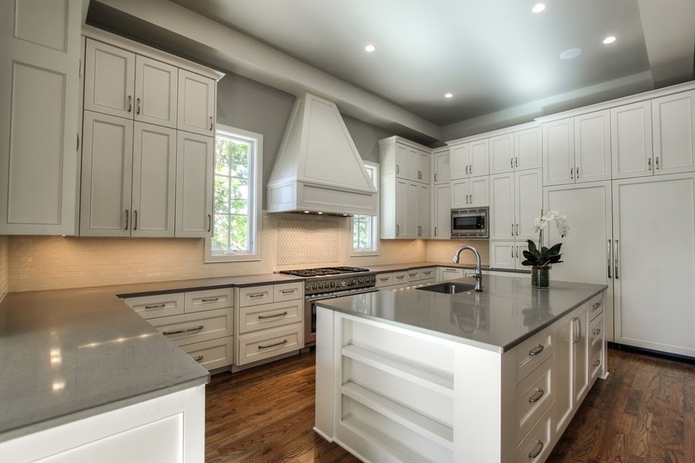 Medium sized traditional u-shaped open plan kitchen in Austin with a submerged sink, shaker cabinets, white cabinets, composite countertops, white splashback, stone tiled splashback, integrated appliances, medium hardwood flooring and an island.